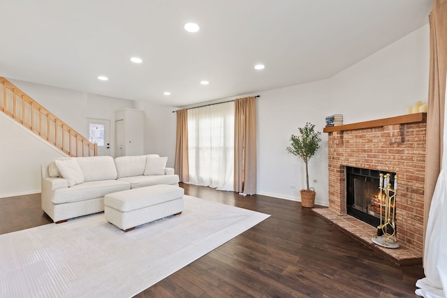 living room with dark wood-type flooring, recessed lighting, stairway, baseboards, and a brick fireplace