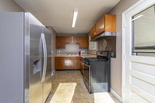 kitchen featuring brown cabinetry, stainless steel appliances, light countertops, under cabinet range hood, and a sink