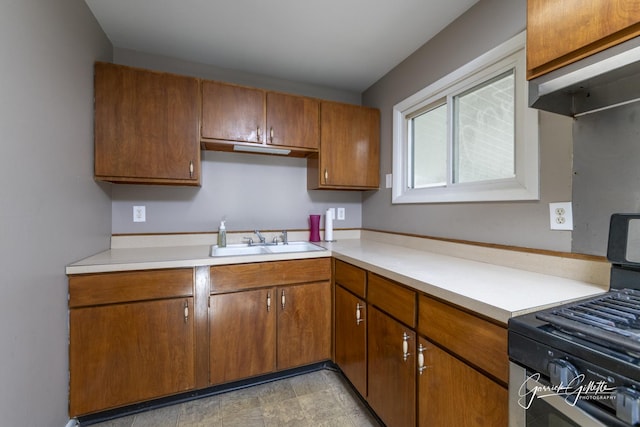 kitchen featuring brown cabinets, gas stove, light countertops, and a sink