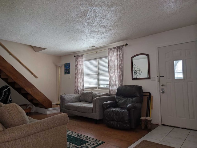 living area with stairs, light tile patterned floors, a textured ceiling, and visible vents