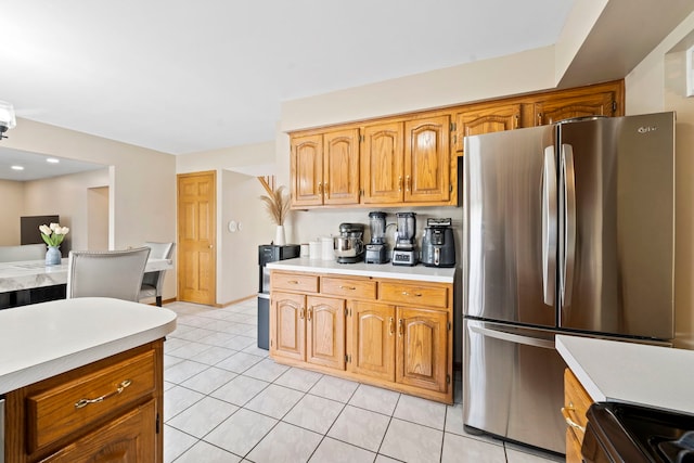 kitchen with electric stove, light tile patterned floors, light countertops, brown cabinetry, and freestanding refrigerator