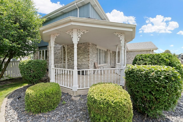 view of side of home featuring a porch, board and batten siding, and brick siding