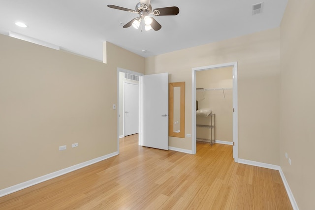 unfurnished bedroom featuring light wood-style flooring, baseboards, and a walk in closet