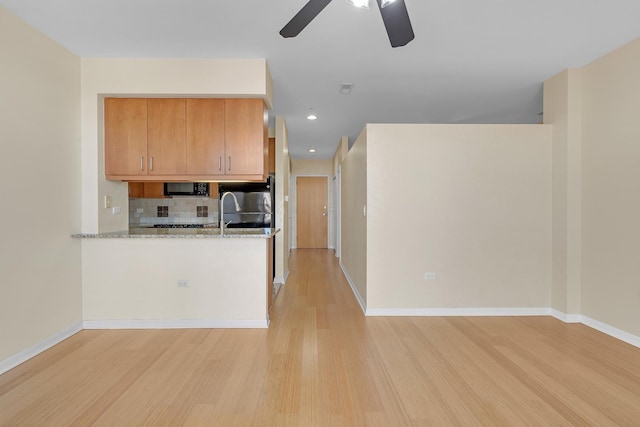 kitchen featuring black microwave, light stone counters, light wood-type flooring, and decorative backsplash