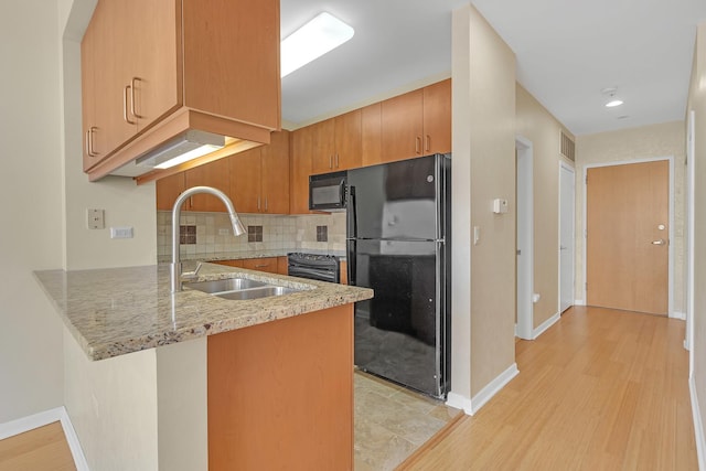 kitchen with a peninsula, a sink, decorative backsplash, light stone countertops, and black appliances