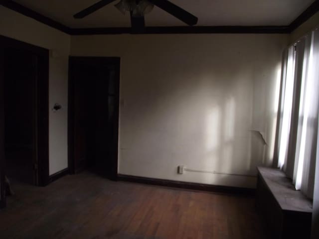 spare room featuring dark wood-style floors, ceiling fan, baseboards, and crown molding