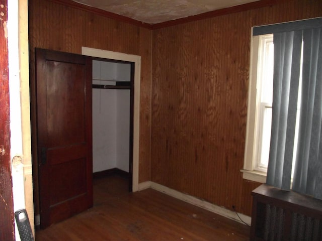 unfurnished bedroom with dark wood-style floors, a closet, wooden walls, and baseboards