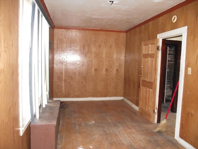 empty room with baseboards, wood walls, wood finished floors, and crown molding