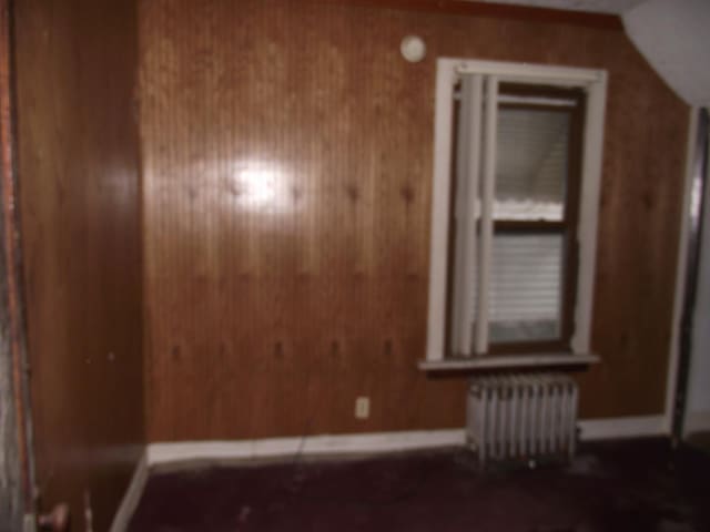 bonus room featuring baseboards, wood walls, and radiator