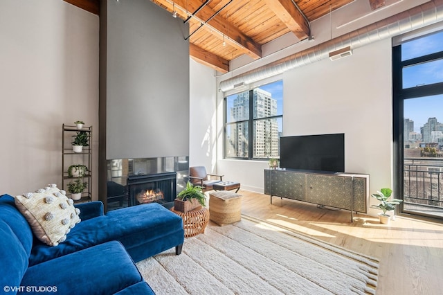 living room featuring visible vents, beam ceiling, wood finished floors, a lit fireplace, and wooden ceiling