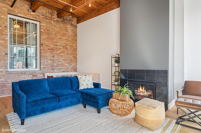 interior space featuring beam ceiling, a tiled fireplace, wood finished floors, brick wall, and wood ceiling