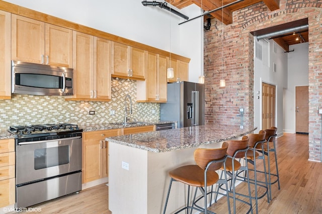 kitchen featuring a kitchen bar, a sink, stainless steel appliances, a high ceiling, and light wood finished floors