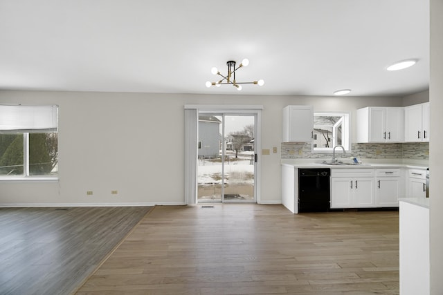 kitchen featuring a sink, backsplash, black dishwasher, light wood-style floors, and light countertops