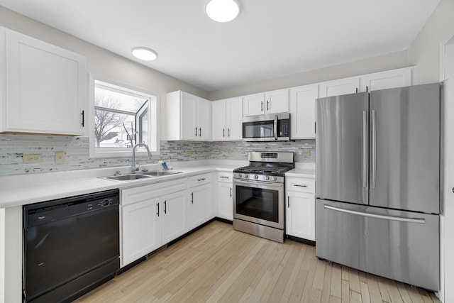 kitchen featuring a sink, backsplash, appliances with stainless steel finishes, light wood finished floors, and light countertops