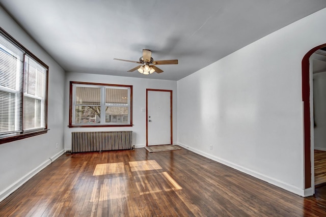 spare room featuring dark wood-style floors, arched walkways, radiator, and baseboards