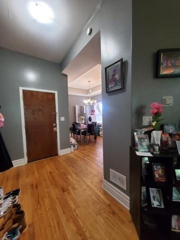 foyer featuring a chandelier, wood finished floors, visible vents, and baseboards