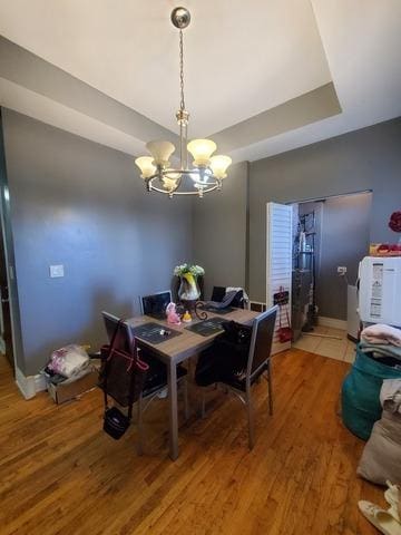 dining space with a tray ceiling, baseboards, an inviting chandelier, and wood finished floors