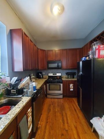 kitchen with black appliances, light stone counters, dark wood finished floors, and dark brown cabinets