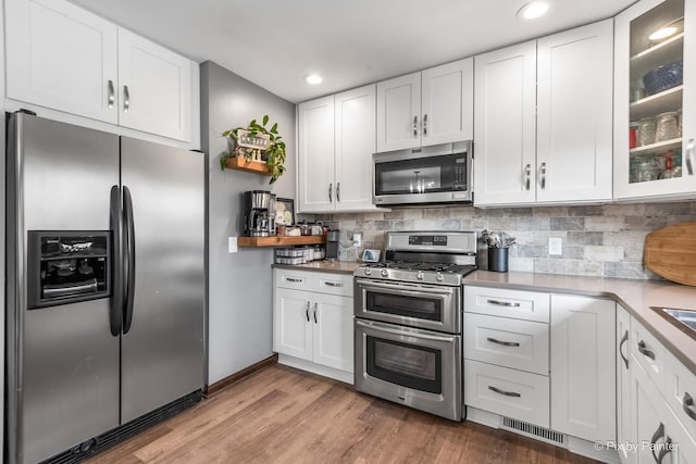 kitchen featuring visible vents, white cabinets, decorative backsplash, stainless steel appliances, and light wood-type flooring