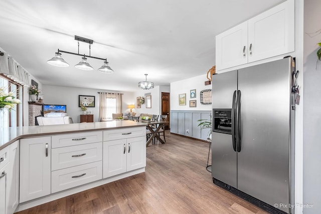 kitchen with a wainscoted wall, white cabinets, stainless steel fridge with ice dispenser, and wood finished floors