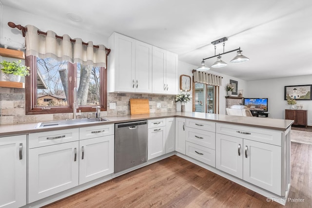 kitchen featuring light wood-style flooring, white cabinetry, a sink, dishwasher, and a peninsula