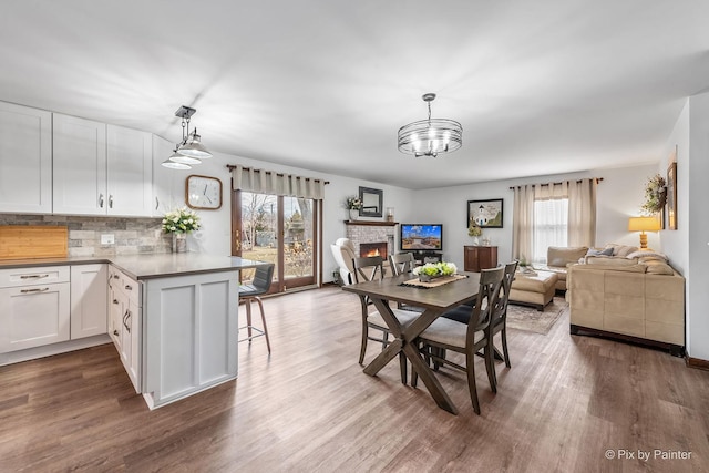 dining space featuring a healthy amount of sunlight, a fireplace, a notable chandelier, and wood finished floors