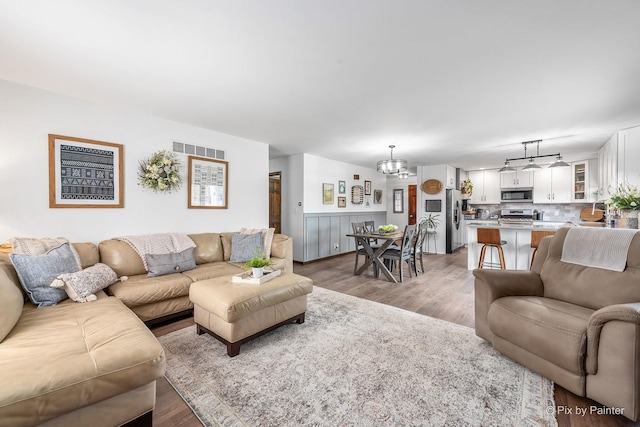 living room featuring light wood-style floors, wainscoting, visible vents, and a notable chandelier