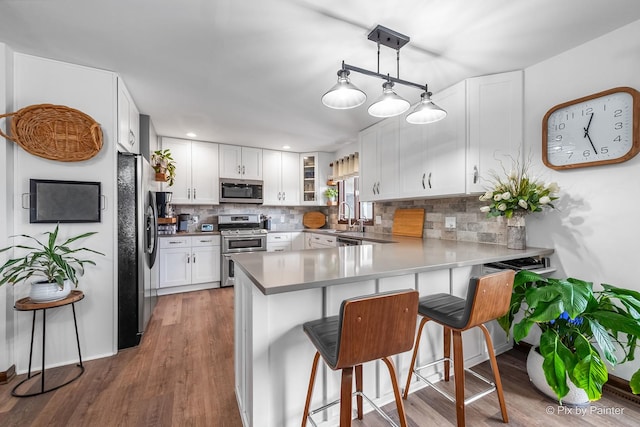 kitchen featuring appliances with stainless steel finishes, white cabinetry, a sink, a peninsula, and a kitchen bar