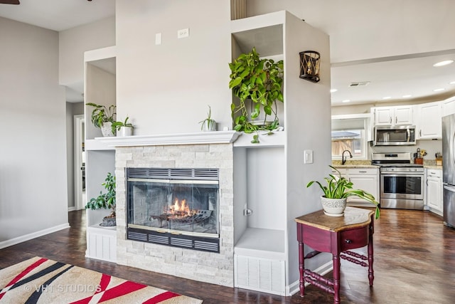 living room with baseboards, visible vents, dark wood finished floors, a stone fireplace, and recessed lighting