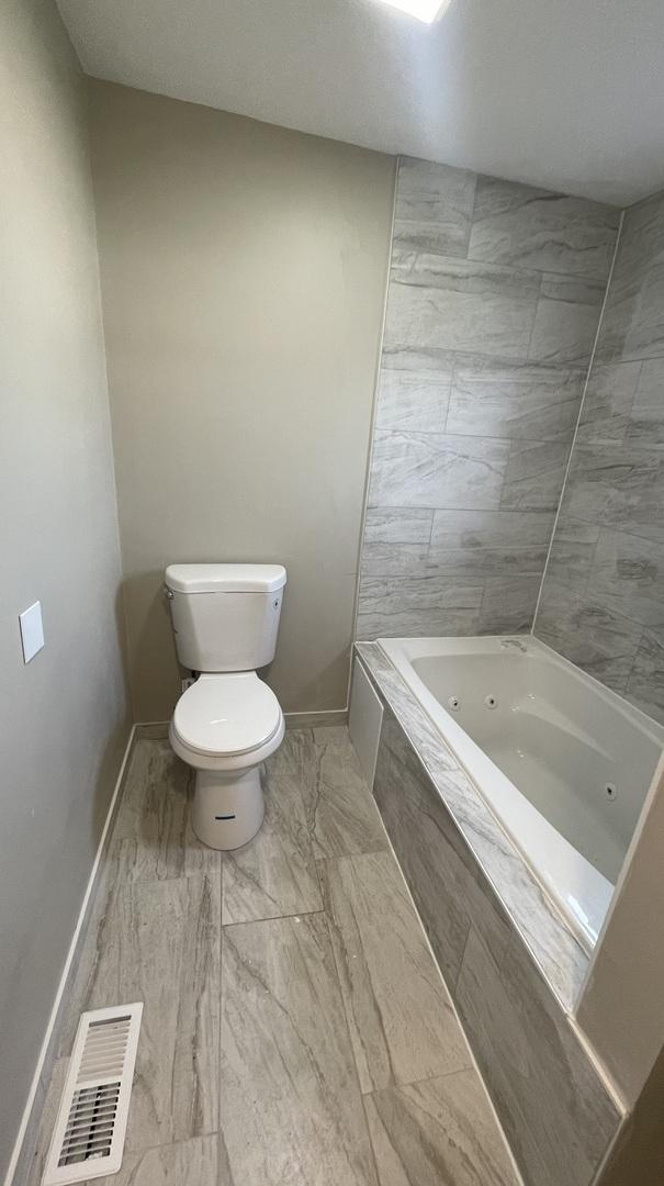 full bath with toilet, a jetted tub, visible vents, and baseboards