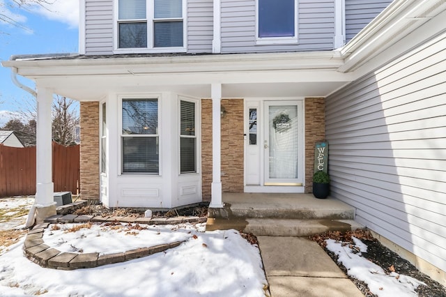 snow covered property entrance with brick siding and fence