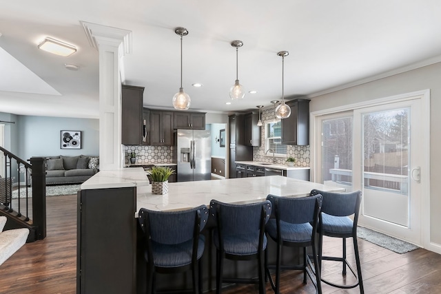 kitchen with tasteful backsplash, appliances with stainless steel finishes, light stone counters, dark wood-style flooring, and a peninsula