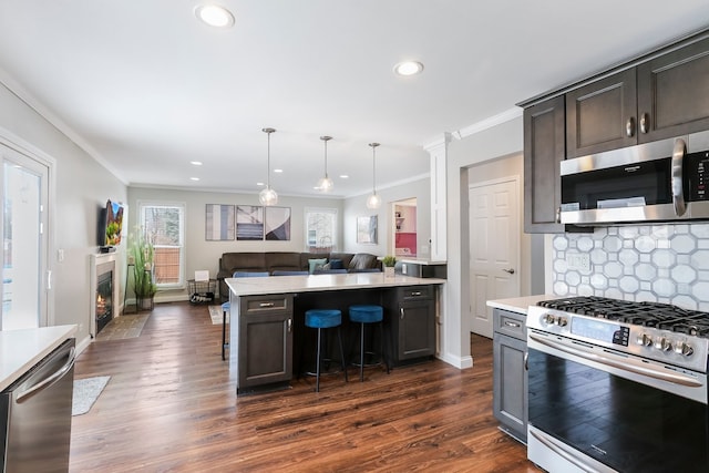 kitchen with dark wood-type flooring, open floor plan, light countertops, appliances with stainless steel finishes, and backsplash