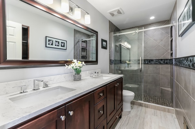 bathroom with toilet, a shower stall, double vanity, and a sink