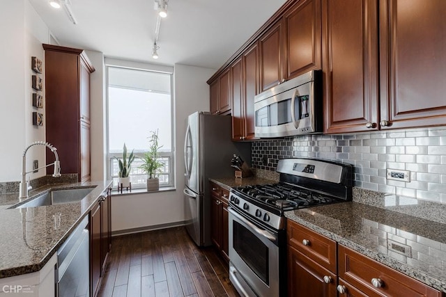 kitchen with stone countertops, dark wood finished floors, decorative backsplash, stainless steel appliances, and a sink