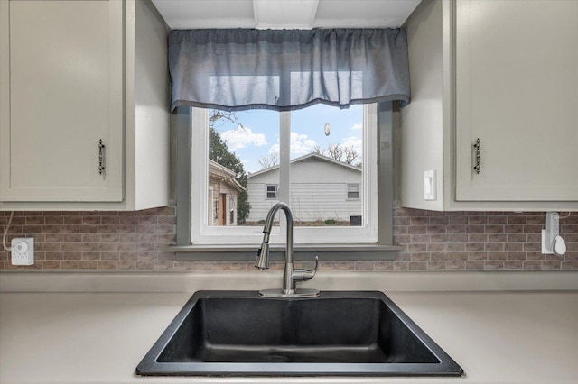 kitchen featuring light countertops, decorative backsplash, a sink, and white cabinets