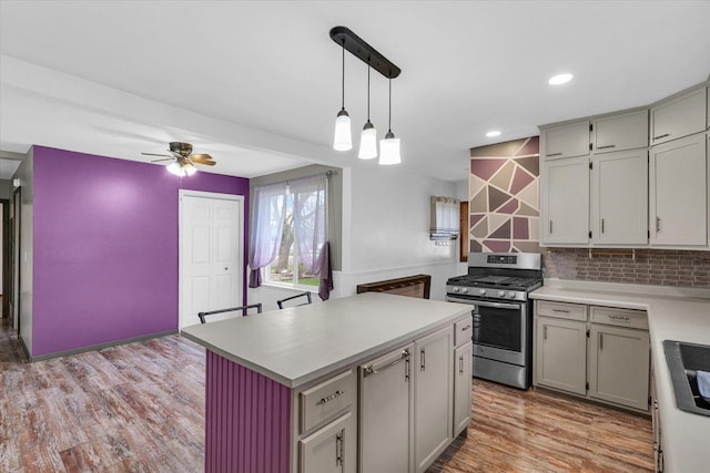 kitchen featuring light countertops, light wood-type flooring, ceiling fan, stainless steel gas range oven, and a kitchen island