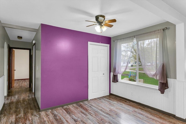 spare room featuring a ceiling fan, wood finished floors, and wainscoting