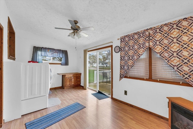 exercise area featuring light wood-style floors, baseboards, a ceiling fan, and a textured ceiling