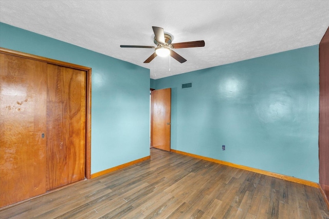 unfurnished bedroom with visible vents, baseboards, a closet, a textured ceiling, and wood finished floors
