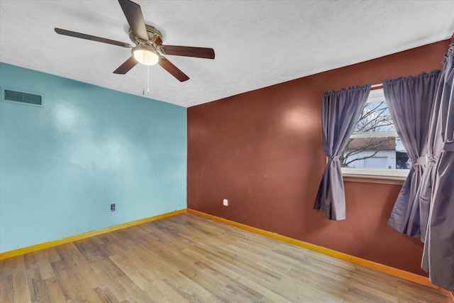unfurnished room featuring a textured ceiling, wood finished floors, baseboards, and visible vents