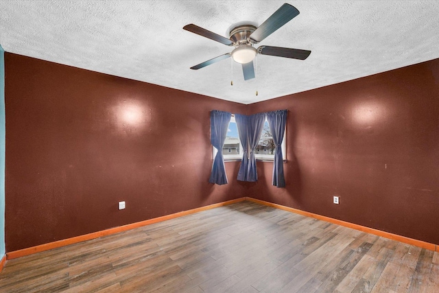 empty room with a textured ceiling, wood finished floors, ceiling fan, and baseboards