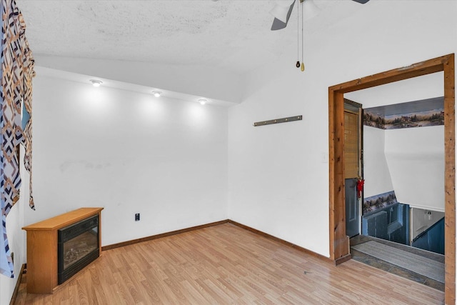 unfurnished room with baseboards, ceiling fan, light wood-style floors, a textured ceiling, and lofted ceiling