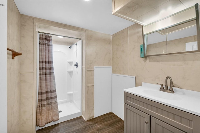 bathroom featuring a stall shower, wood finished floors, vanity, and tile walls