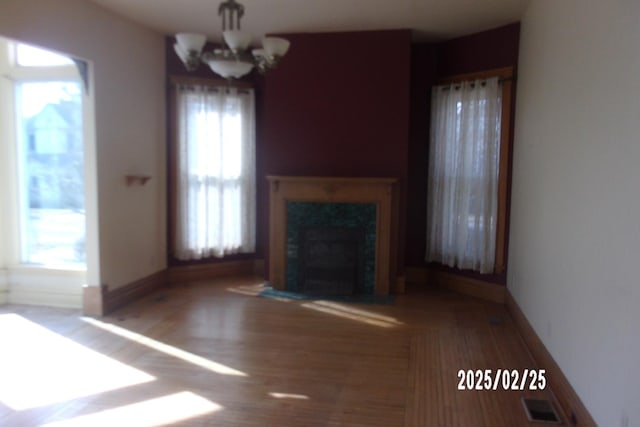 unfurnished living room with a premium fireplace, wood finished floors, visible vents, baseboards, and an inviting chandelier