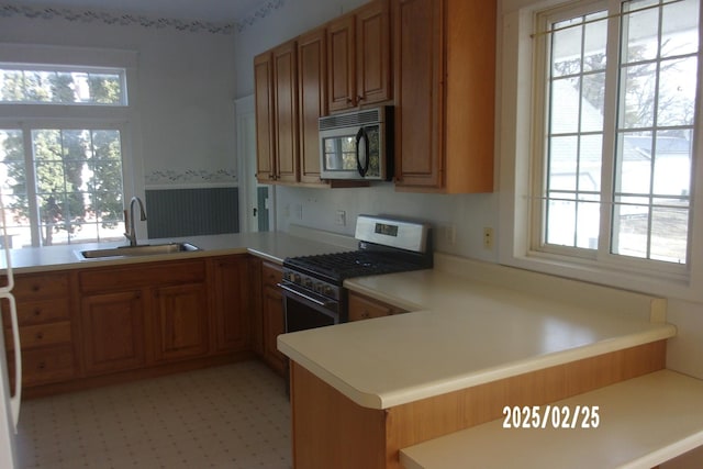 kitchen with a peninsula, a sink, light countertops, stainless steel gas range, and brown cabinets