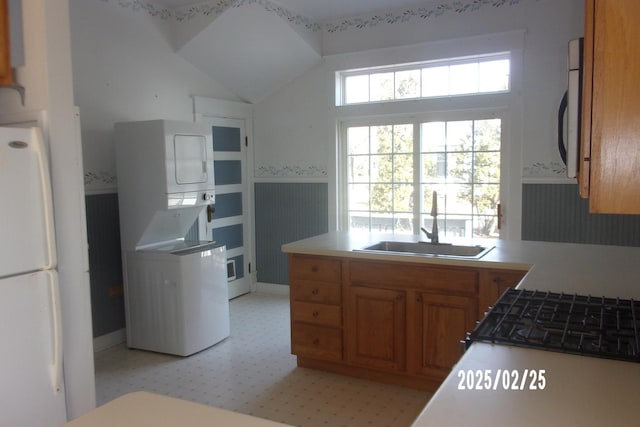 kitchen featuring a wainscoted wall, stacked washer / dryer, a sink, light countertops, and brown cabinetry