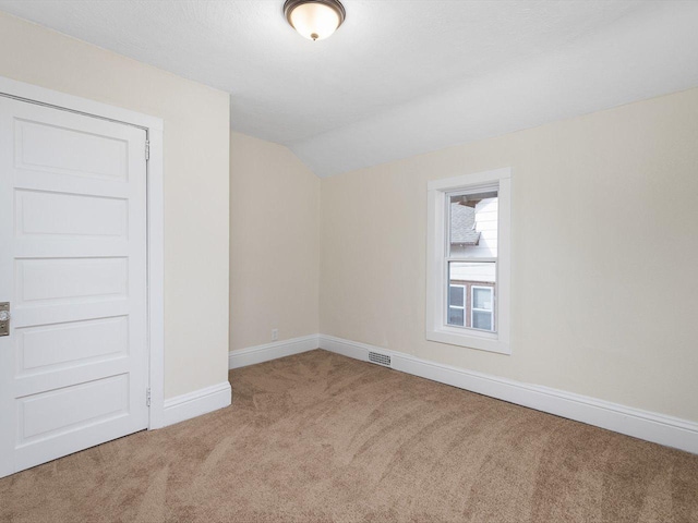 unfurnished room with carpet flooring, vaulted ceiling, visible vents, and baseboards