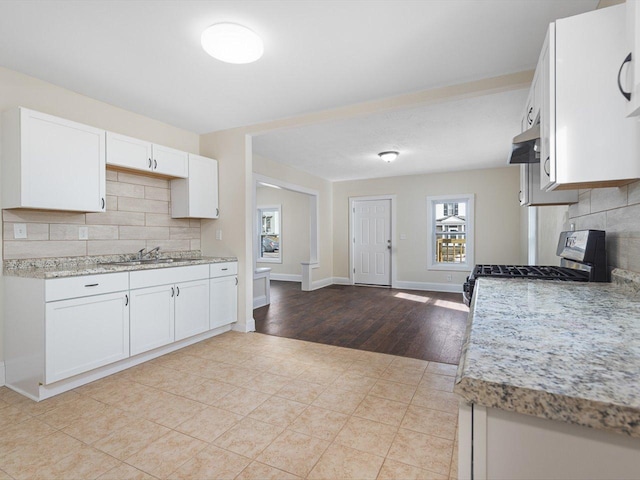 kitchen featuring baseboards, decorative backsplash, gas range, under cabinet range hood, and white cabinetry