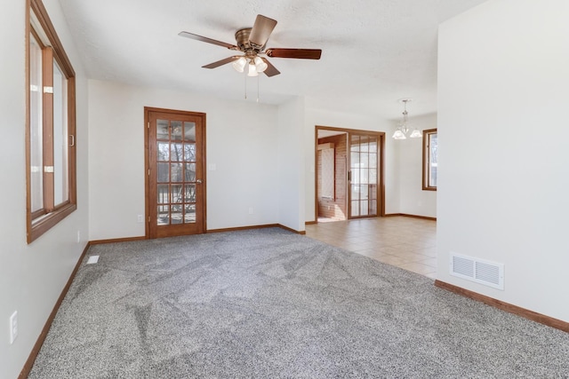 carpeted spare room with baseboards, visible vents, tile patterned flooring, and ceiling fan with notable chandelier